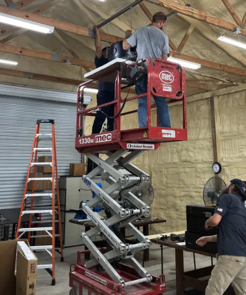 Two ACE technicians on a scissor lift installing equipment in a spray-foamed warehouse